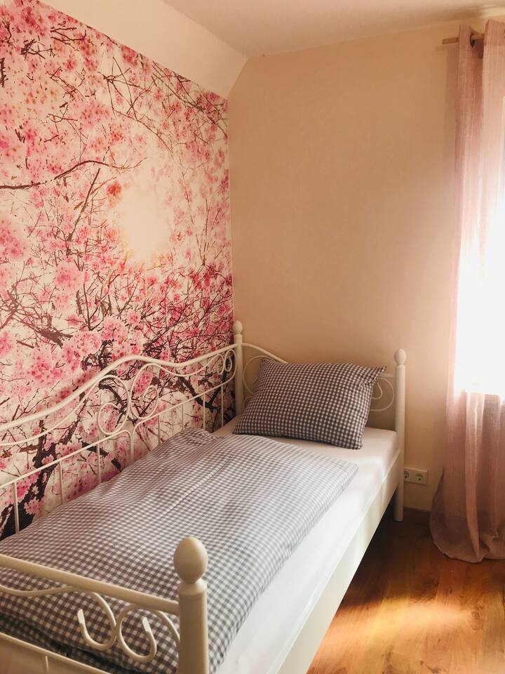 Dormitorio con cama individual y decoración de pared con cerezos en flor