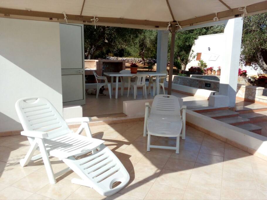 Portico esterno con zona relax,tavolo e sedie e in fondo angolo cottura all’aperto