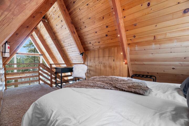 This mountain-facing view from the loft shows the king-sized bed, string lights, closet, luggage racks and desk.

The desk has a leather chair, fur throw, charging station & work light.  It looks out on the mountains and makes work more relaxing.