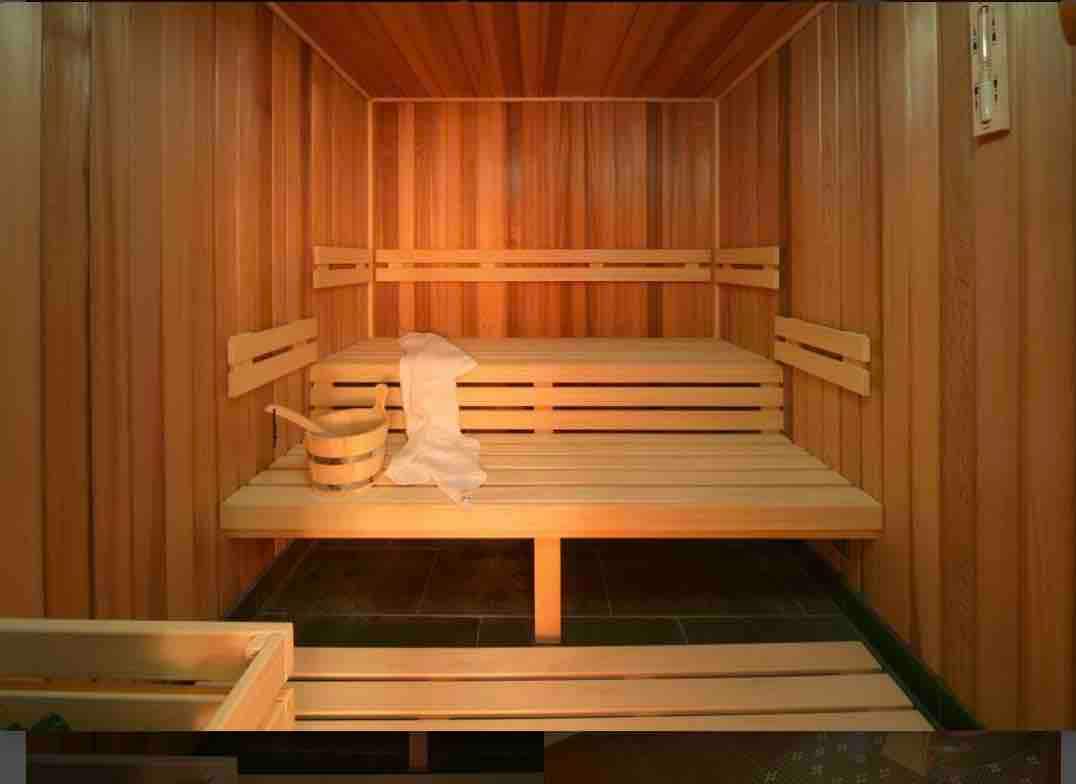 A wooden sauna interior features warm, light wooden benches arranged along the walls. A light-colored towel and a wooden bucket are placed on one of the benches. Soft lighting creates a serene environment suitable for relaxation.