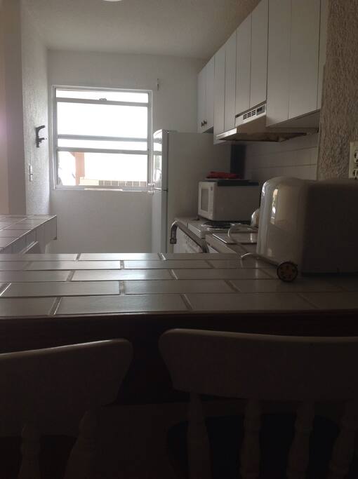 A fully equipped kitchen. Fridge, stove, microwave, toaster, pot, pans cutlery, dishes and glasses.