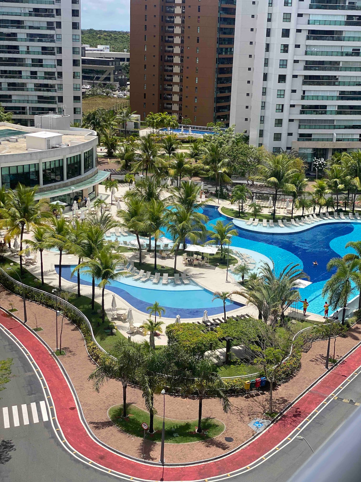 An aerial view of a resort-style pool area is displayed, featuring multiple swimming pools in varying shades of blue. Palm trees are strategically placed around the pools, with lounge chairs arranged nearby, creating inviting spaces for relaxation.