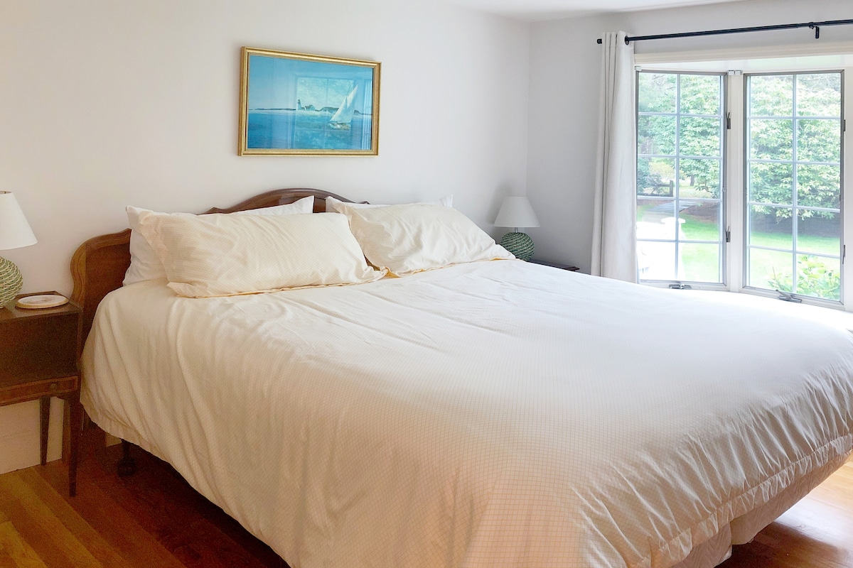 Cette chambre dispose d'un lit king size, d'une baie vitrée avec siège, d'un placard avec des étagères et un espace suspendu, de deux commodes, d'un bureau et d'une chaise.