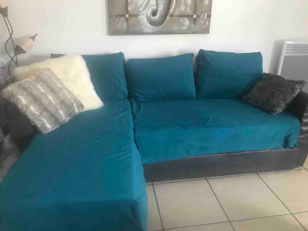 A modern sectional sofa is presented in a teal fabric with various decorative pillows. The arrangement showcases a cozy seating area, complemented by an adjacent wall art piece featuring subtle colors and patterns.
