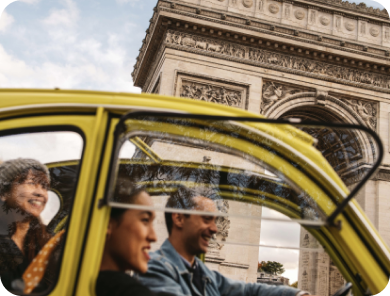 Hosts riding in a small yellow car with the Arc de Triomphe visible in the background.
