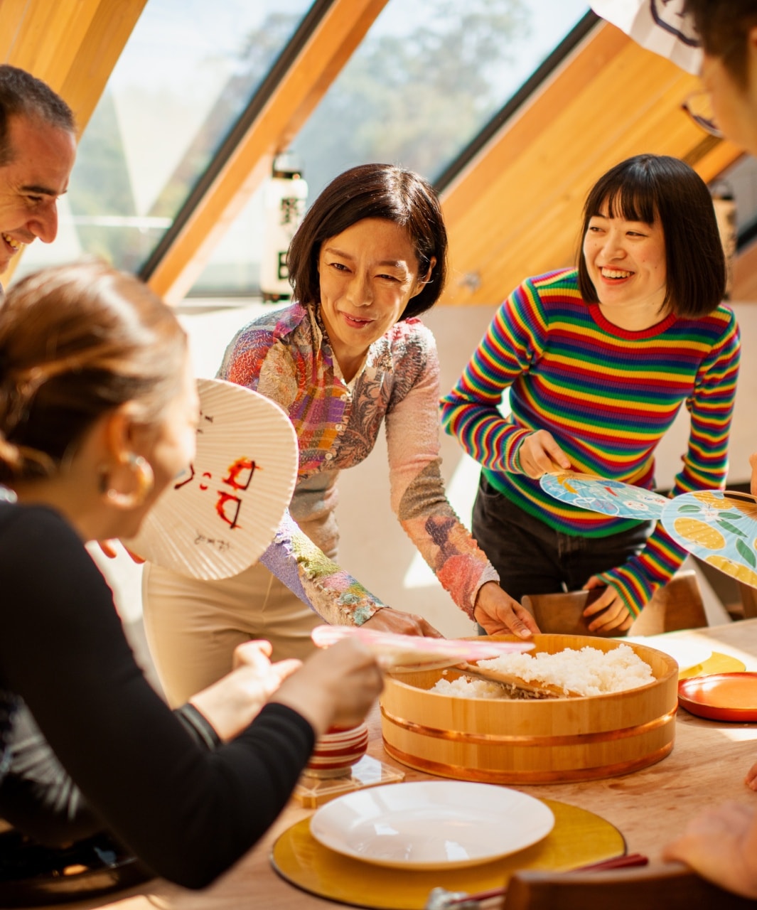 Host leading a hands-on cooking activity with guests gathered around a table preparing food.