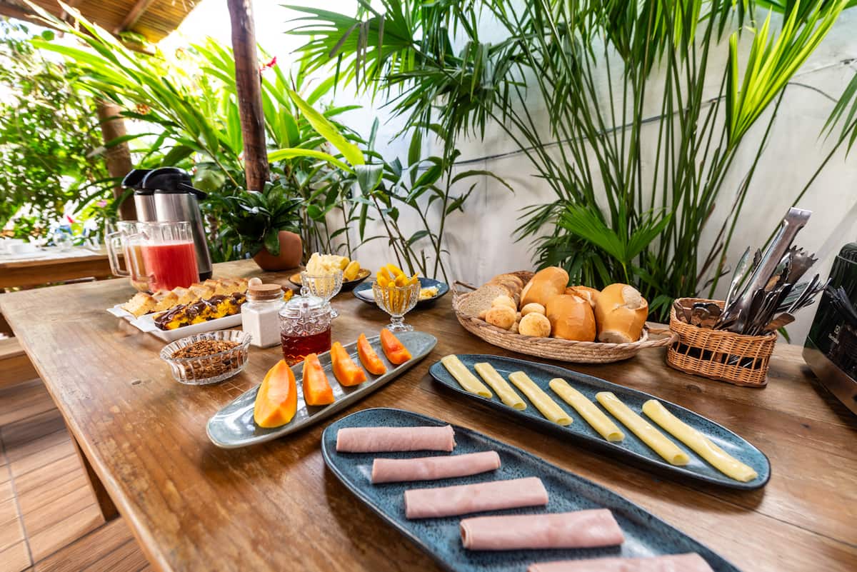 Mesa do café da manhã da Casa Maruê: mamão, frios, pães e bolos no jardim