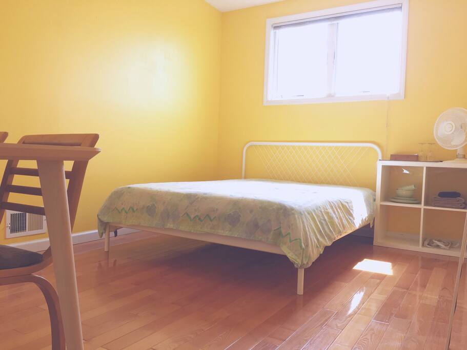 This is a bright, large room featuring a table/desk with two chairs, a queen-sized bed, hardwood floors, a simple shelving unit, silverware/dishes and a drying rack for towels (which we provide). As it is down its own little hallway it is our most private room! perfect for travelers who want to save money and spend their time out in New York!