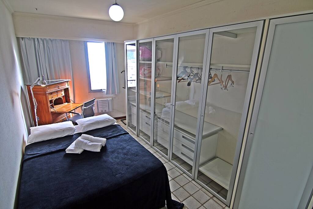 Quarto com cama de casal, ar condicionado, armários e mesa de trabalho.