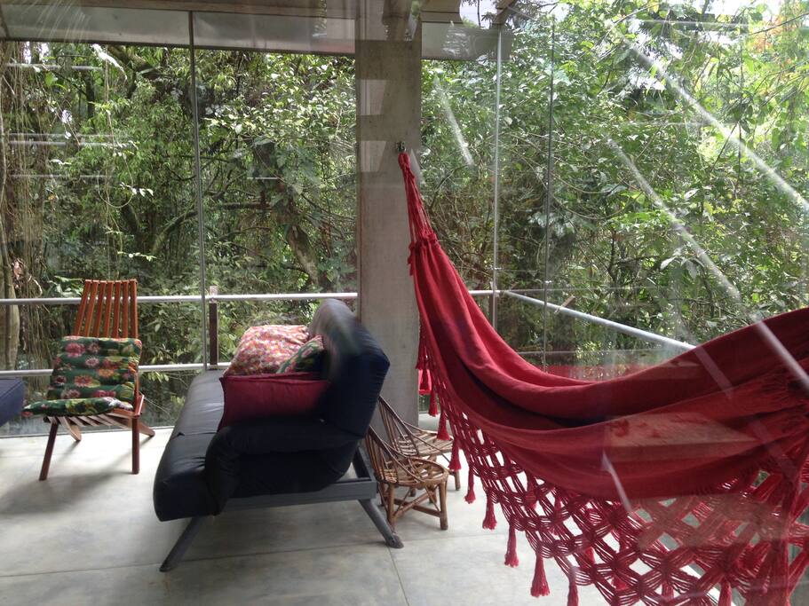 Sala e cozinha com paredes de vidro, vista para mata