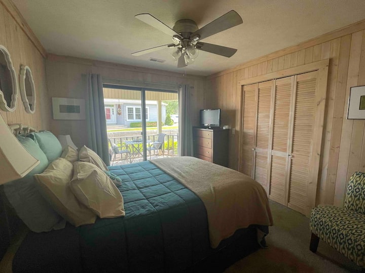 غرفة نوم بمقاس كبير في الطابق الأول.  يفتح شريط التمرير على الشرفة المغطاة.  رائعة لتناول القهوة الصباحية أو المشروبات في نهاية اليوم.  تلفزيون بشاشة مسطحة. شعور مريح مع ألواح الصنوبر. 