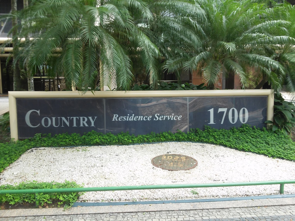 A large sign displaying 'Country Residence Service 1700' is set against a backdrop of lush greenery and rounded stones. The area is well-maintained, with manicured plants and grass, contributing to a welcoming entrance.