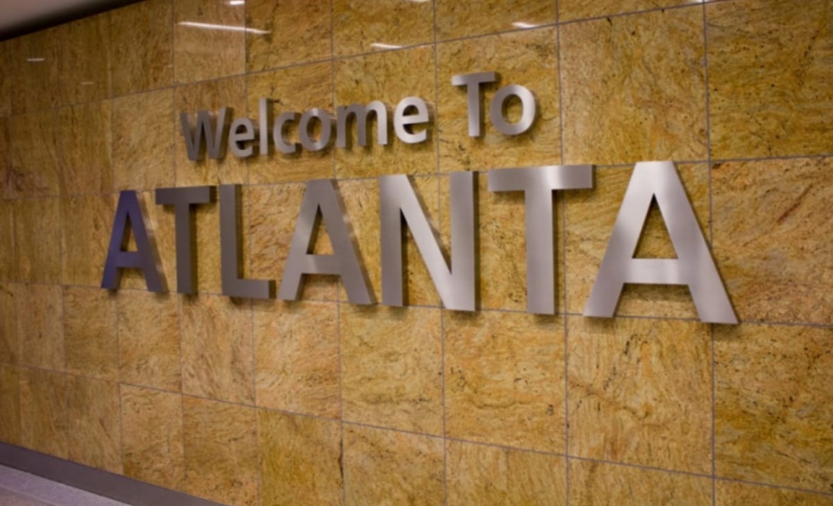 A large metallic sign is mounted on a smoothly finished stone wall, displaying the welcoming message 'Welcome To ATLANTA.' The warm tones of the stone enhance the welcoming ambiance of the space.