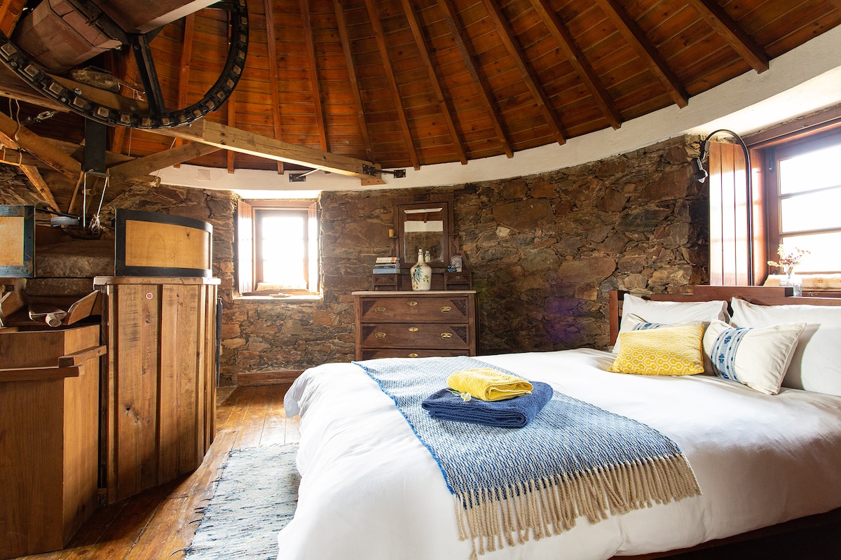 A kingsize bed in the upstairs bedroom with windows showing 360 degree views of the countryside