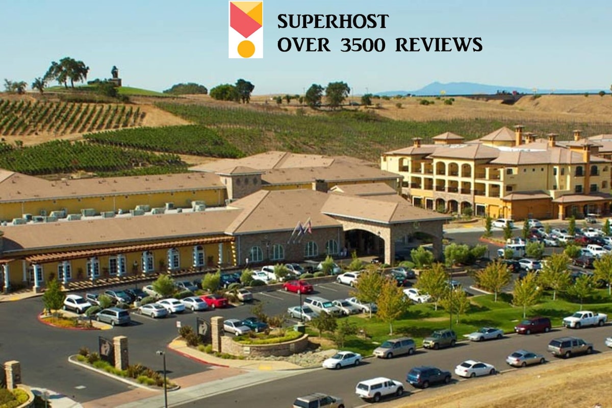 The resort is depicted from an elevated viewpoint, showcasing its expansive grounds and well-maintained landscaping. Multiple vehicles are parked in front, with the scenic vineyard hills visible in the background against clear skies.
