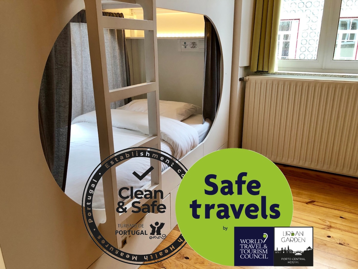 A cozy sleeping capsule is shown, featuring a spacious bed within a rounded alcove. Soft curtains frame the entrance, offering privacy. Warm wooden flooring contrasts with the light-colored walls, creating a welcoming environment. Certification logos for safety and cleanliness are displayed prominently.