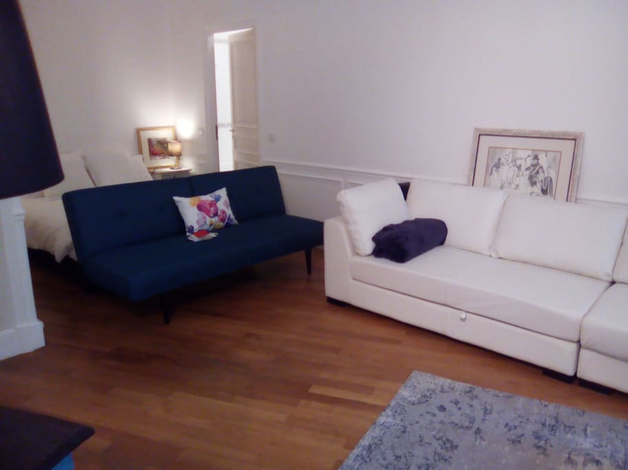 Extended versatile studio layout with central space available to open table at entrance. Blue clic-clac available as single bed. 2 adjacent white leather sofas are each convertible to small double beds.