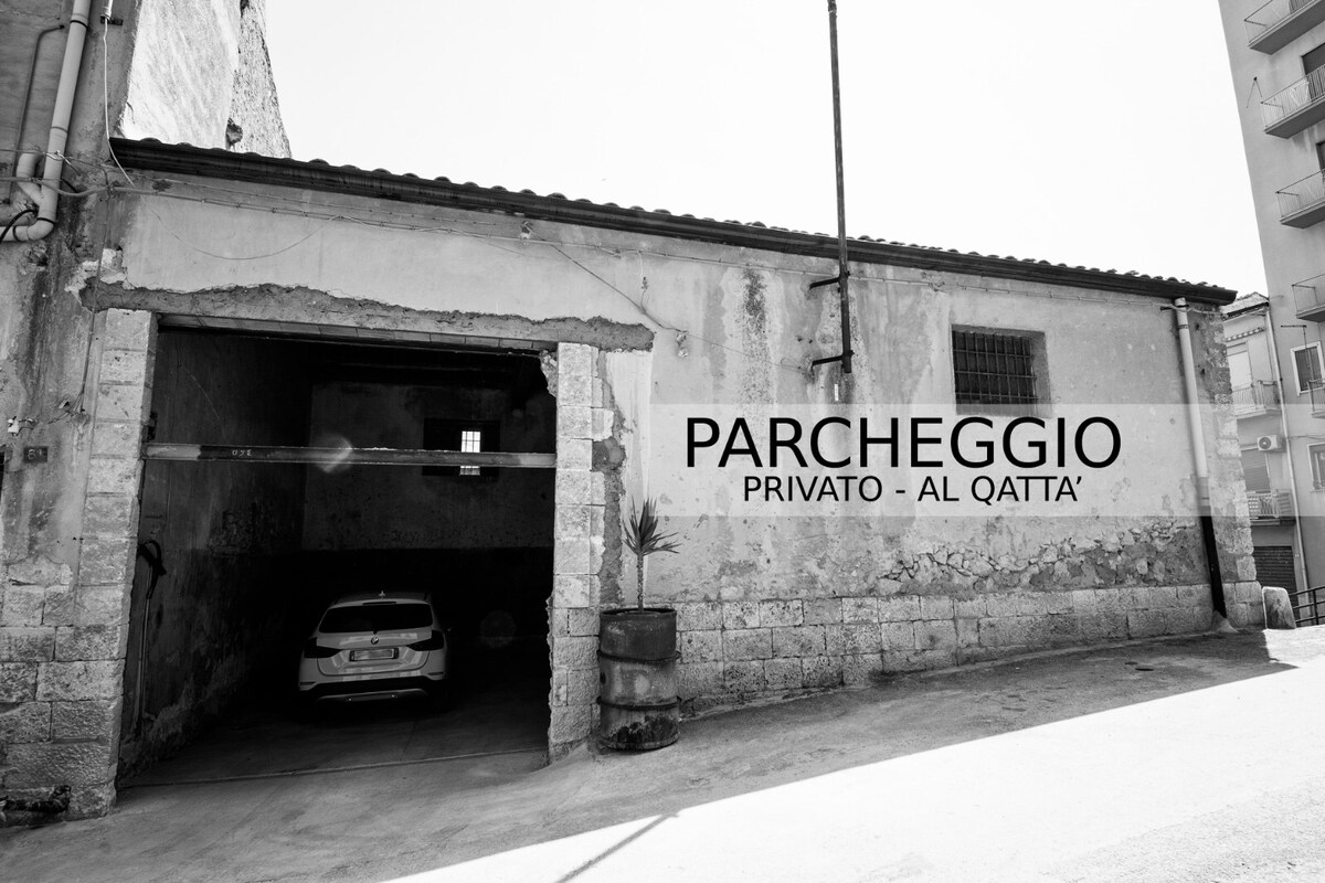 A private parking area is shown, featuring an enclosed space with a door open to reveal a parked vehicle. The surrounding walls exhibit a rustic texture, with items for storage positioned nearby.