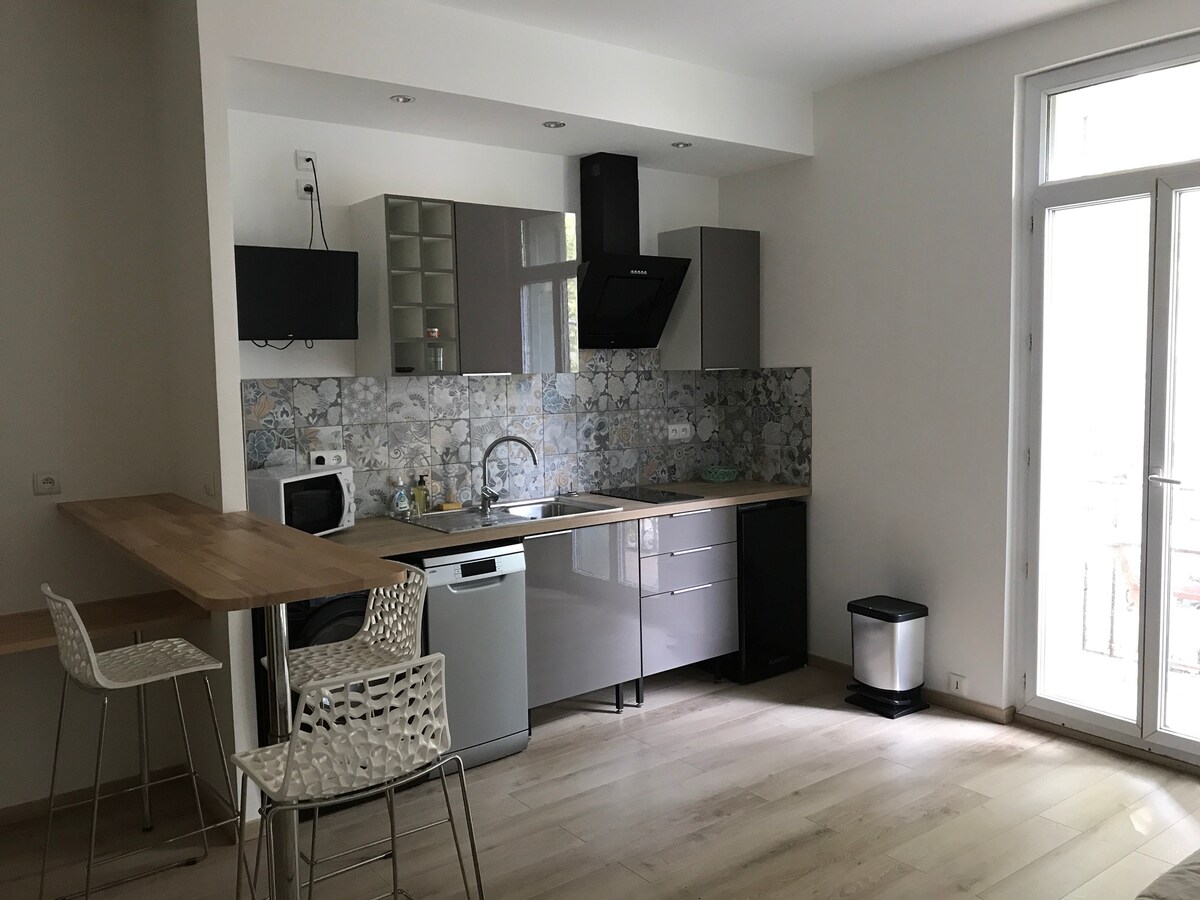 A modern kitchen layout is displayed, featuring sleek cabinetry and a stylish countertop with bar seating. Kitchen appliances, including a microwave and a dishwasher, are clearly visible. Natural light filters in through a glass door leading to a small balcony.