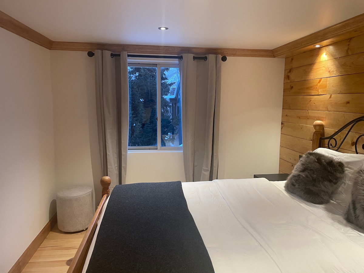 כריות פרווה של שועל ופוף עור פרה בחדר שינה גדול יותר. נוף של עצי אורן, מבריח והר אדום מאחור.