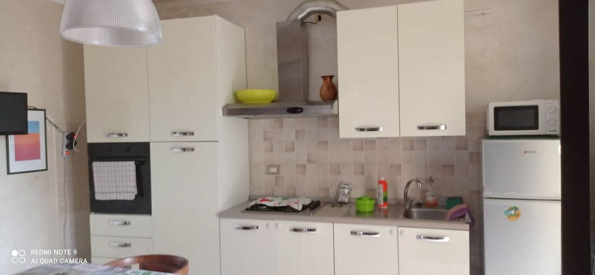 A compact kitchen area is equipped with essential appliances, including a stove, oven, and microwave. Cabinets and countertops in neutral tones provide adequate storage and preparation space. Brightly colored dishes and utensils add functional elements to the kitchen, enhancing its practical appeal.