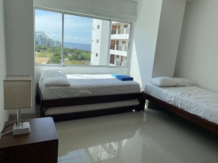 ห้องที่สองพร้อมเตียงเดี่ยวสองเตียงและเตียงเดี่ยวเสริม หน้าต่างวิวทะเลพร้อมม่านสีเข้ม ตู้เสื้อผ้าขนาดใหญ่โต๊ะกลางคืนพร้อมโคมไฟนาฬิกาปลุกและสายเคเบิลสำหรับชาร์จไฟฟ้าเครื่องปรับอากาศ