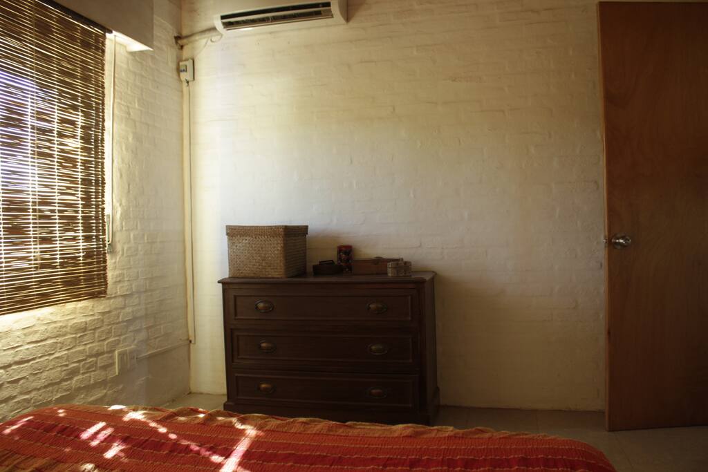 Dormitorio con cama doble, ropa de cama, cómoda, mesitas de luz, aire acondicionado.