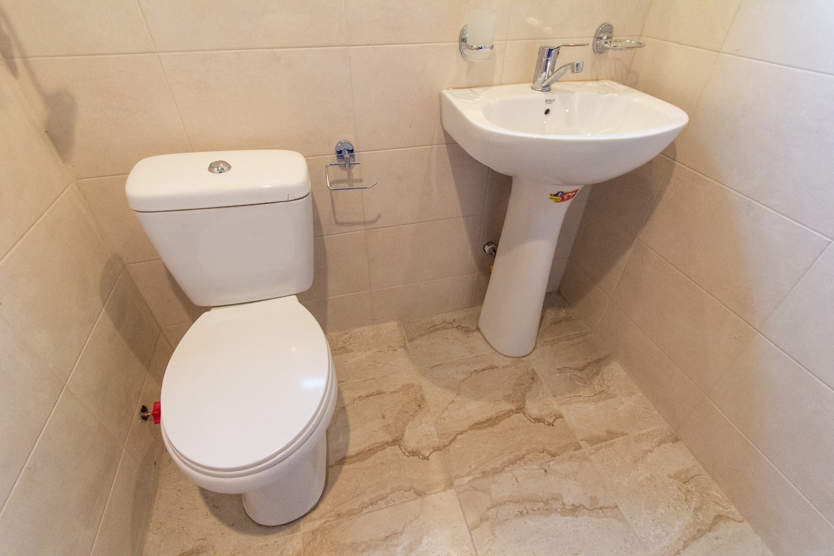 The bathroom features a modern toilet and a sleek sink with a polished faucet. Neutral-toned tiles cover the walls and floor, contributing to a clean and minimalistic design.