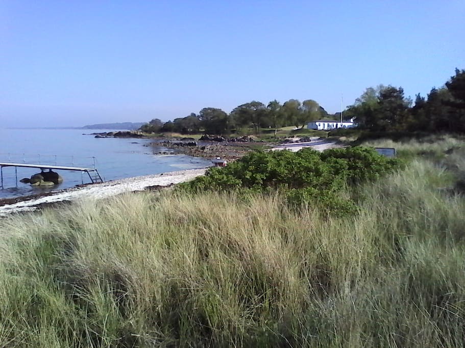 Stranden med badebro, ligger ca 100 m. fra huset og med naboen Melsted Badehotel i baggrunden,