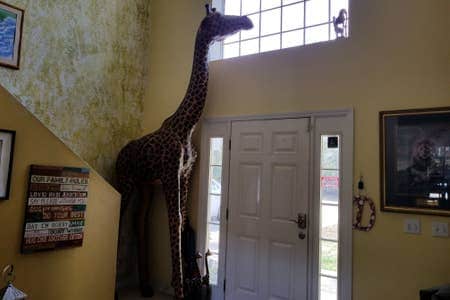 A tall giraffe statue is positioned near the front door, reaching towards a window above. The walls are painted in a soft yellow hue, enhancing the bright entrance area. A framed artwork is displayed on the wall, contributing to the inviting ambiance.