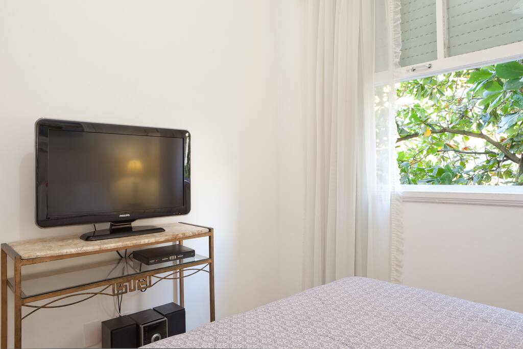 Quarto com TV e janela com paisagem para as árvores