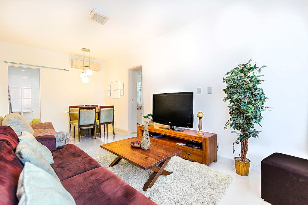 Large, modern, spacious living room area with open dining room, Plasma TV, Split Air-conditioning unit, tan sofa is folds out into sofa bed.