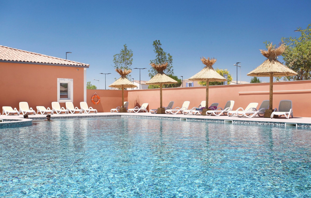 A bright outdoor pool area is surrounded by a sun deck featuring numerous lounge chairs arranged neatly under straw umbrellas. The crystal-clear water reflects the blue sky, inviting relaxation in a comfortable and open setting.