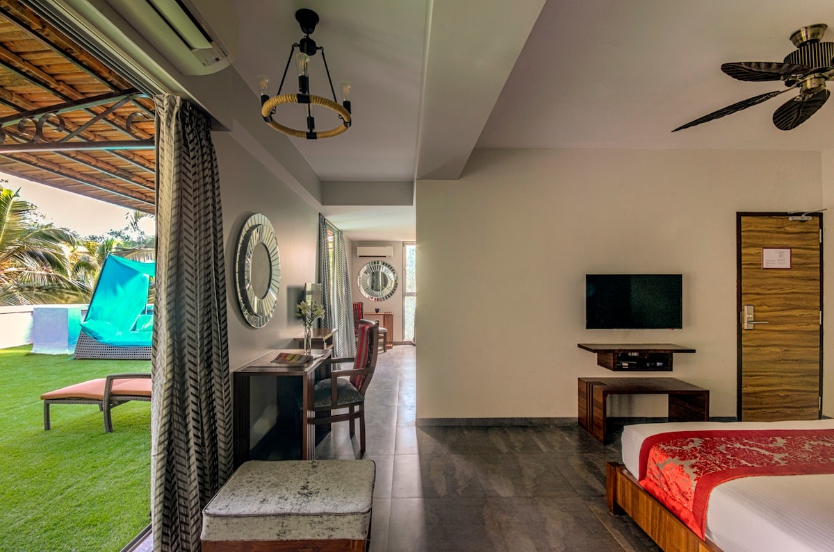 A spacious master suite is featured, showcasing a comfortable bed with crisp linens. A large window offers views of a private terrace garden, while a flat-screen TV and a modern desk enhance the interior. Natural light fills the room, complemented by stylish decor elements.