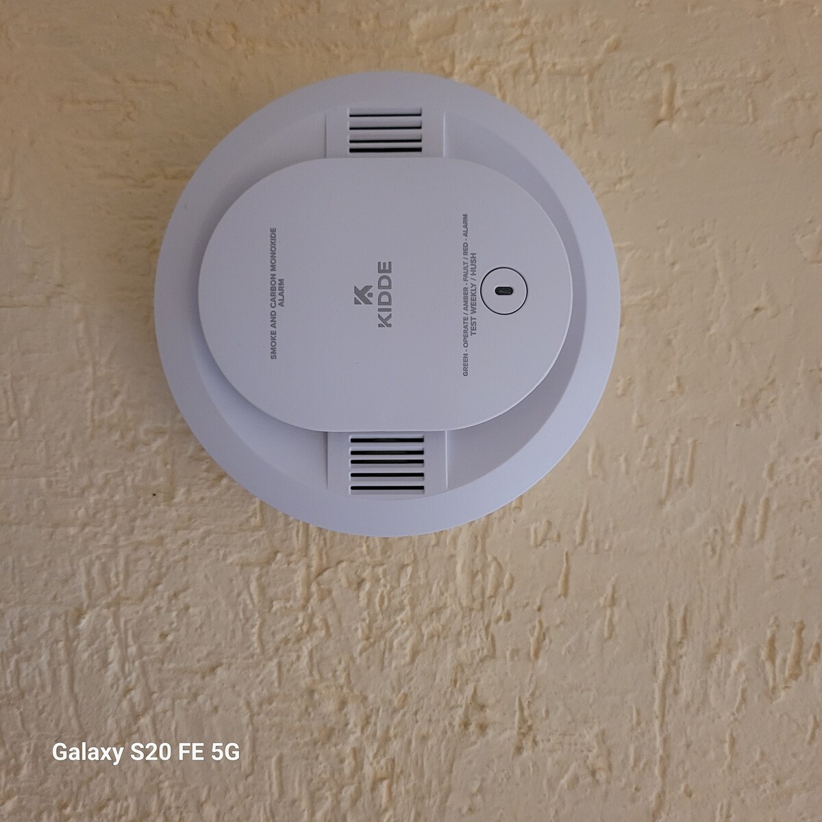 A smoke detector is mounted on a textured wall, featuring a circular design with ventilation slots. The detector is prominently positioned, ensuring safety in the living space.