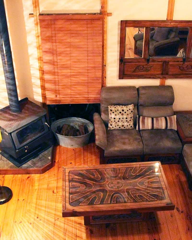 A comfortable seating area is showcased with a plush couch, accented by decorative cushions. A wooden coffee table featuring a distinct design is positioned in front of the couch. A wood-burning stove is visible, contributing to the cozy ambiance.