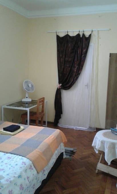 There's a desk with a chair and a fan, curtains to give some privacy when door to the patio is open, double wardrobe with hangers and a bed./
Uma escravininha com cadeira, venitaldor, guardaroupa, cortinas para a porta para dar privacidade quando abrir a porta da varanda, uma mesinha e uma cama.