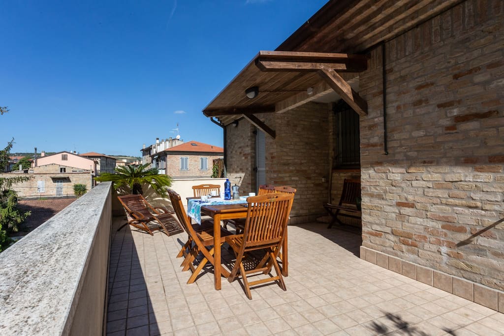 Il grande terrazzo con tavolo per 6 persone, chaise longue, panca e tettoia.