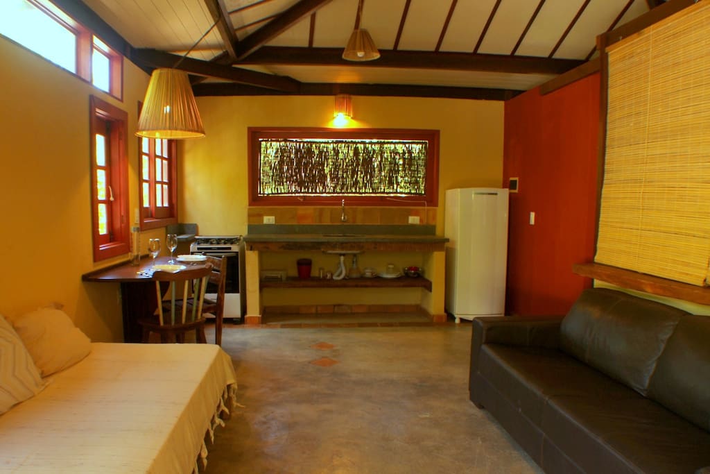 Vista da sala estar/jantar (com cama solteiro e sofá) e da cozinha