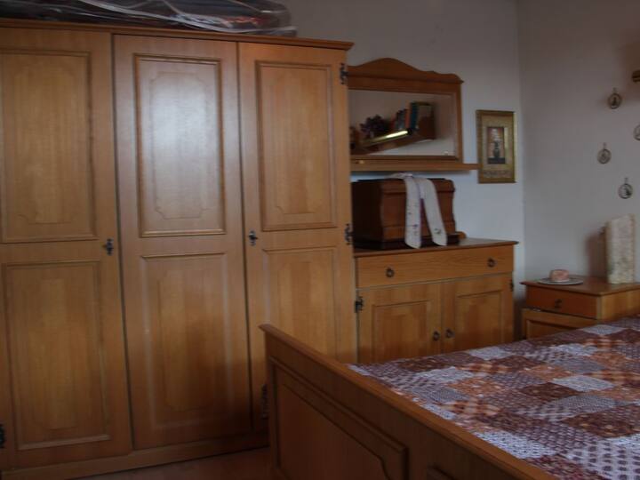 Dormitorio en planta baja con aspecto rústico de granja, cama doble de 1,80 m de ancho con marcos de pizarra ecléctica, amplio armario, cajonera,mesitas de noche