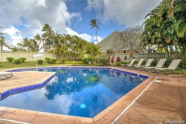 A refreshing swimming pool is surrounded by palm trees and lush landscaping. Lounge chairs are neatly arranged on the pool deck, inviting relaxation. The clear blue water reflects the sky, enhancing the serene setting.