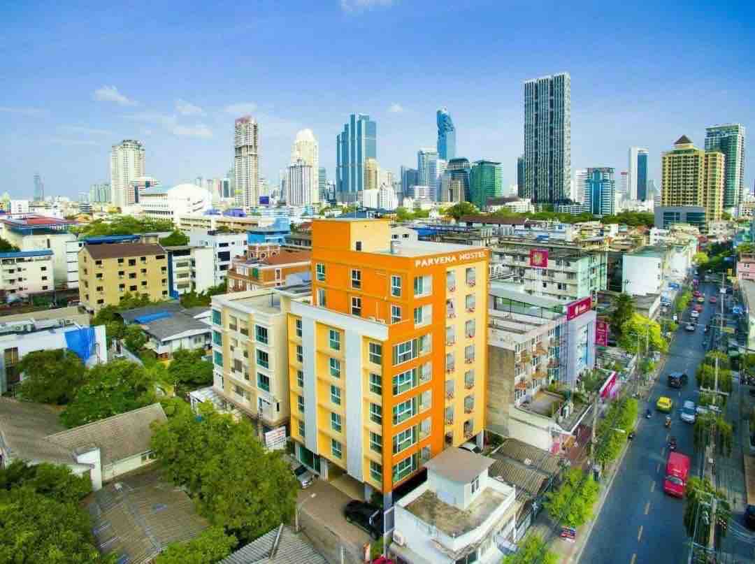 Aerial view of Parvena Hotel presents a vibrant orange and beige building among a cityscape featuring modern skyscrapers. The bustling street below is lined with greenery and residential buildings, highlighting the hotel's urban setting.