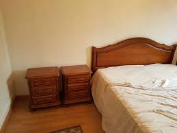 A calming bedroom features a spacious bed with a light-colored coverlet. Two wooden nightstands are placed symmetrically on either side of the bed. The floor is covered with light wood, and a simple area rug adds a touch of warmth to the space.