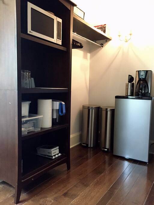 Large walk in closet includes food prep area with microwave, mini fridge, mobile cart with cutting board surface, coffee maker and other kitchen amenities.