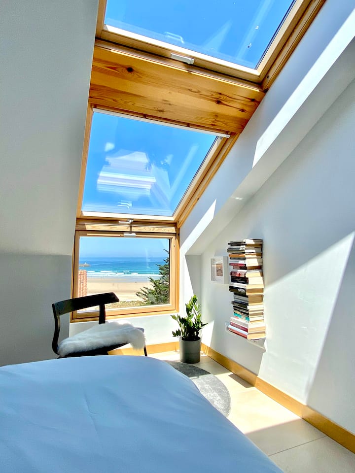 לופט עם חדר שינה זוגי עם חלונות לתקרה שבו אפשר לראות את הים.