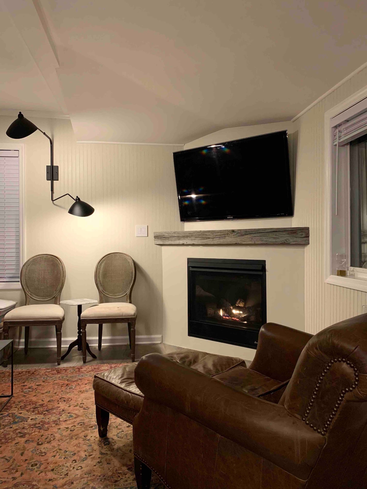 Нощна снимка на всекидневната с камина. Камината е включена чрез превключвателя за осветлението, монтирано на стената, вляво от камината. Превключвателят за включване / изключване, както и управлението на вентилатора на камината са лесно достъпни и контролирани. 