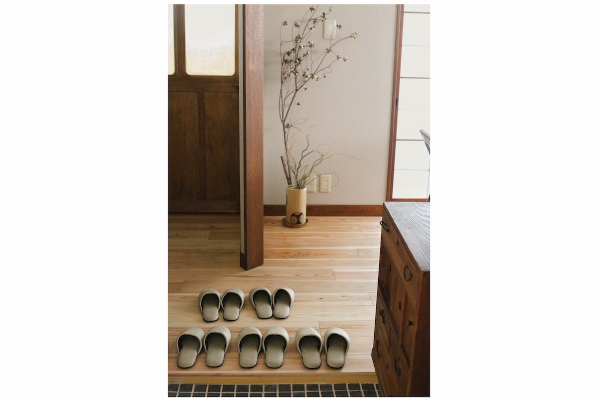 A welcoming entrance area features a wooden floor with traditional slippers arranged neatly. A decorative branch stands in a simple vase, adding a natural touch to the space. The wooden door frame and flooring enhance the cozy ambiance of the apartment.