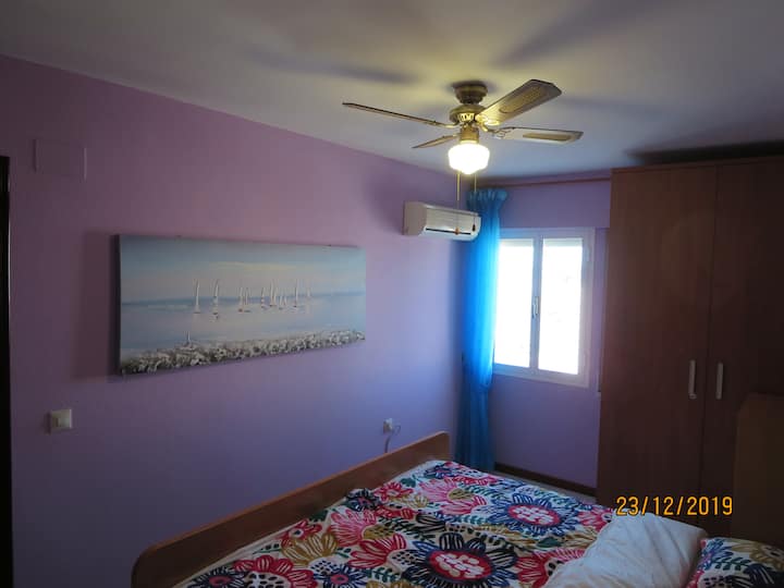 Dormitorio con cama doble, ventilador de techo y aire acondicionado.
