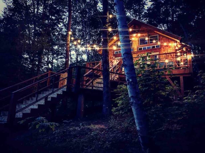 A treehouse in Vermont with twinkle lights hung outside and a long staircase leading up to it