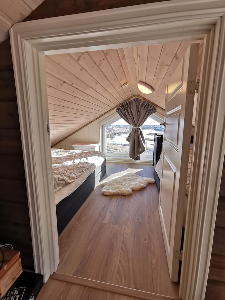 Habitación 3
En el ático hay una habitación aislada con 2 camas dobles de 150 cm de ancho. También hay una cama de bebé, que se puede mover a una de las otras habitaciones si lo deseas. Puede hacer calor aquí en los días más calurosos de verano, luego te recomendamos que abras las ventanas de arriba y la puerta del porche de abajo para que obtengas buenas corrientes de aire. 
Aproximadamente 175 cm de altura hasta el techo en el centro. Preciosa vista del centro de Brasøy.